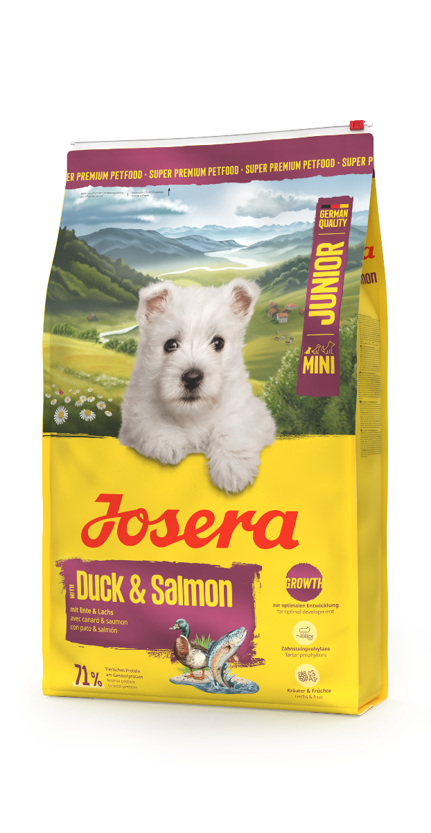 Verpackung von Josera Mini Junior mit Ente & Lachs für Welpen kleiner Hunderassen. Zeigt niedlichen weißen Welpen auf gelbem Futtersack mit ländlichem Hintergrund.